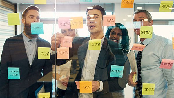 3 men in suit looking at an agile board with sticky notes